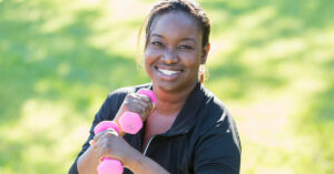 Mature African American woman (40s) in park, exercising with hand weights.