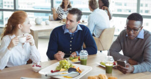 colleagues from mixed race backgrounds indulging in lunch in a contemporary office space. Seated at a table, engaging in conversation about the election and appreciating shared moments.