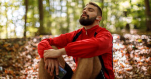 Portrait of relaxed young man with bluetooth headphones in forest