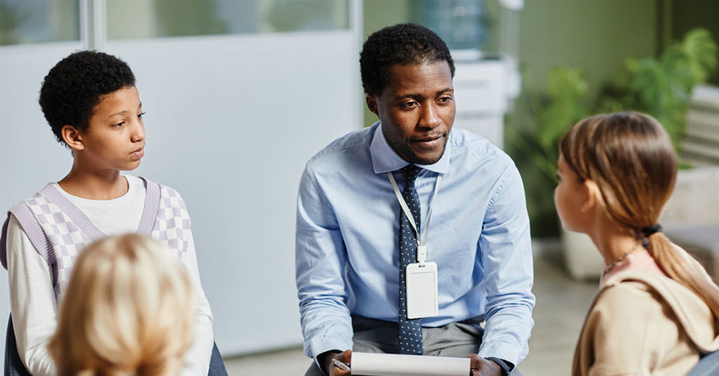 Portrait of young African-American psychologist listening to children in support group circle